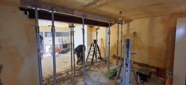 Stalen ligger boven een brede wandopening, met tijdelijke stempels en werkzaamheden in de ruimte.