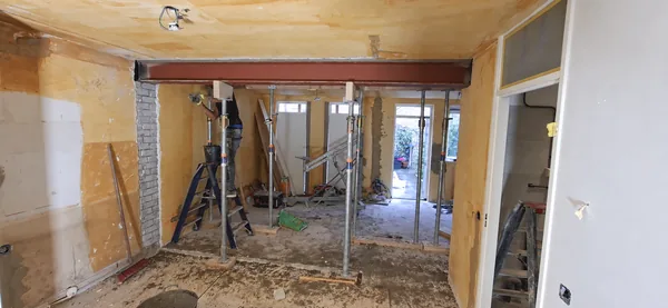 Vooraanzicht van een wandopening met een rode stalen ligger, stempels en een monteur.