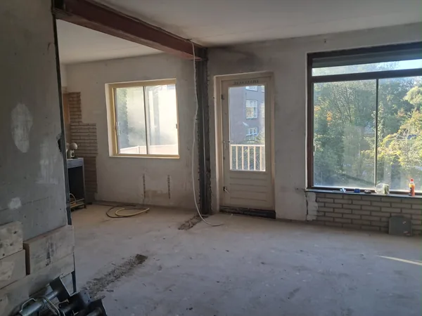 Zijaanzicht van een rode stalen ligger en donkere kolom in een woning in verbouwing.