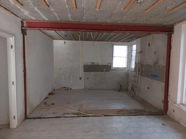 Rood stalen raamwerk in een geopende binnenwand van een woning in verbouwing.